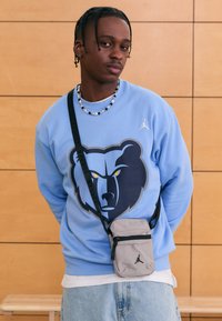 Világoskék pulóver medve grafikával, világoskék farmerral párosítva. Szürke válltáska fekete cipzárral és logó részlettel.