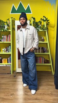 Ruuduline triiksärk beeži ja valge toonides, laiad sinised teksad, valged tossud ja tumesinine nokamüts. Taustal kollased seinad ja rohelised riiulid.