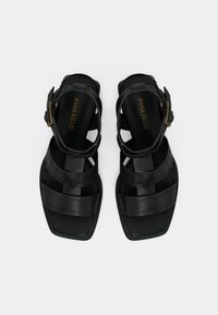 Μαύρα δερμάτινα σανδάλια με σχεδιασμό από λουράκια, τετράγωνη μύτη και χρυσή αγκράφα για ρυθμιζόμενη εφαρμογή. Ματ υφή στην επιφάνεια.