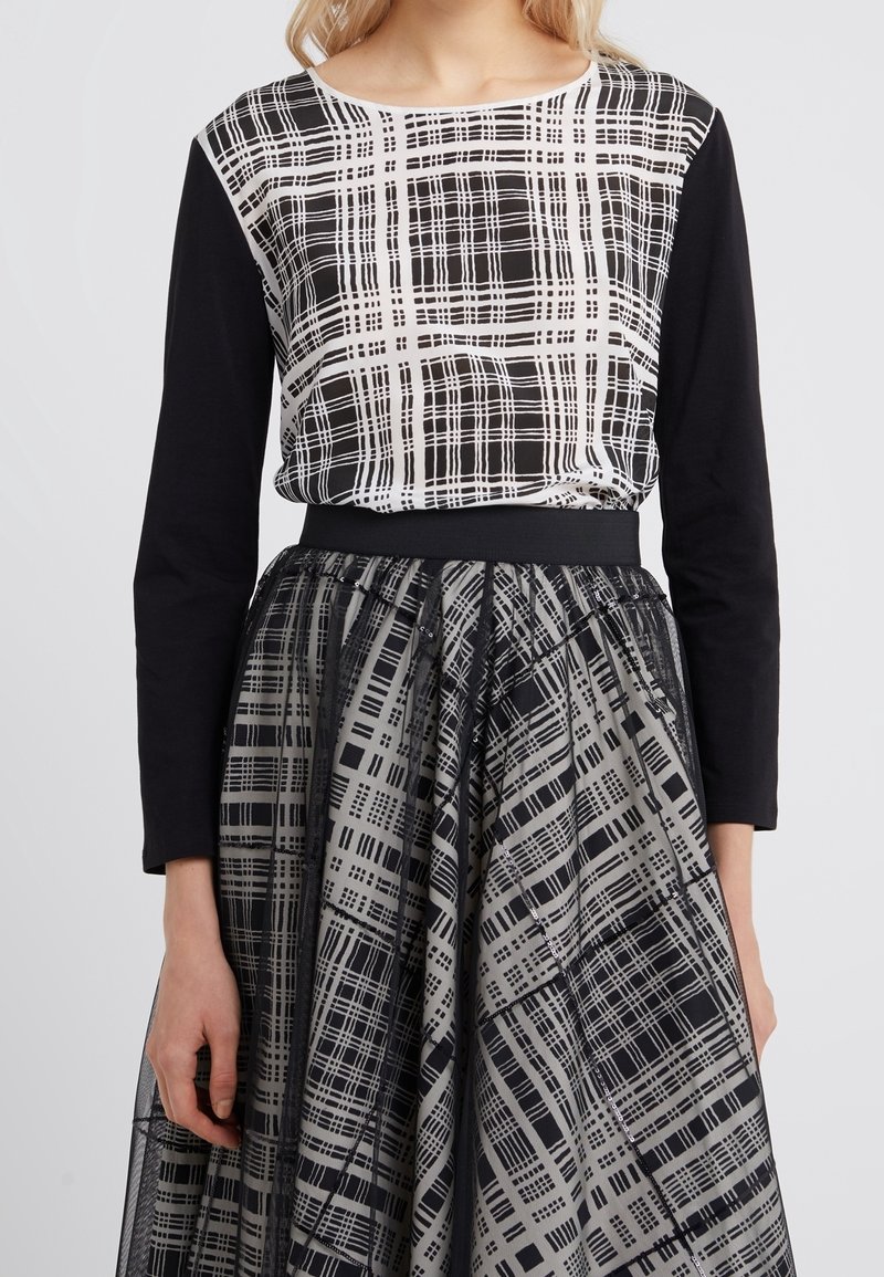 Woman wearing black long-sleeve top with white and black grid pattern and matching patterned flared skirt with sheer overlay.