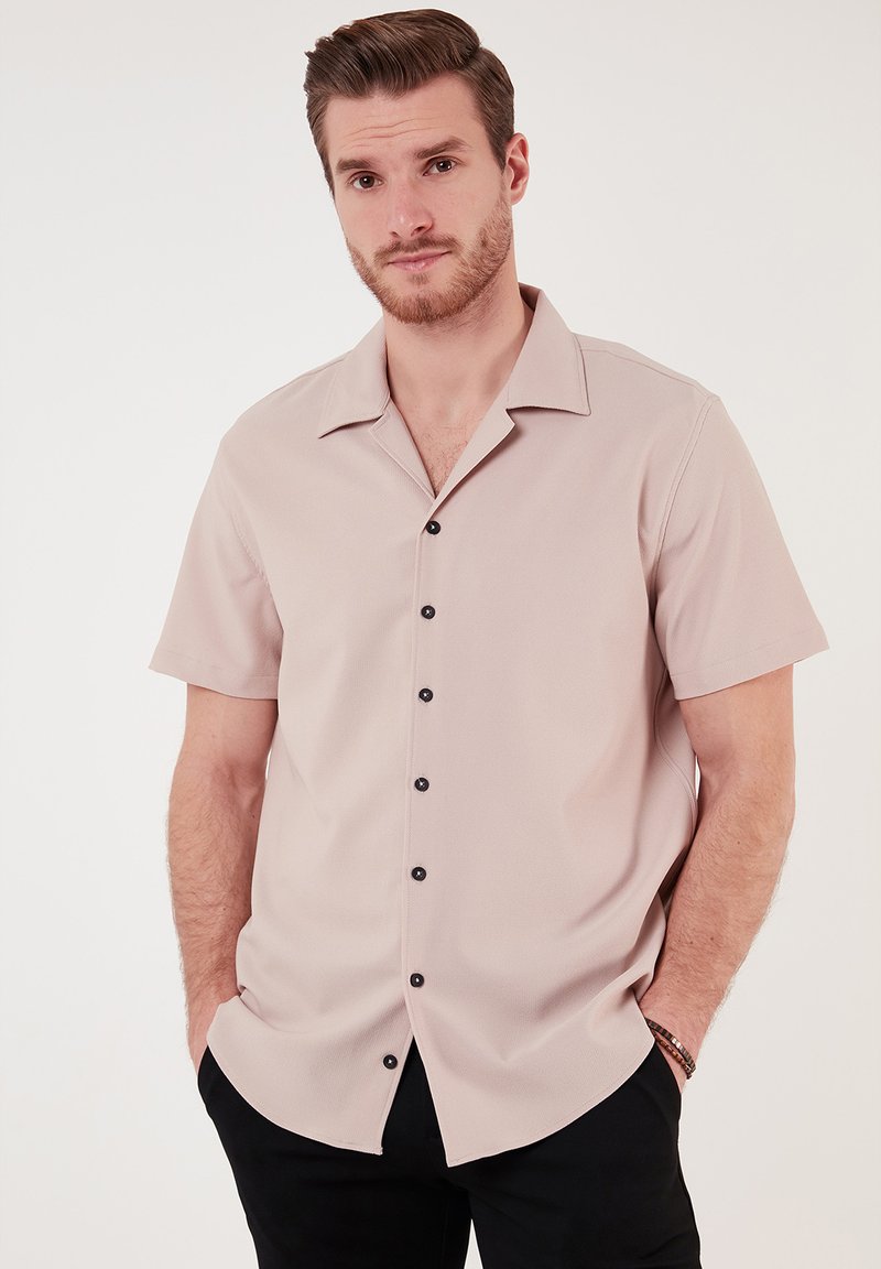 Lichtroze korte mouwen shirt met een relaxte pasvorm, voorzien van een kraag en zwarte knopen aan de voorkant. Zachte textuur, casual ontwerp.