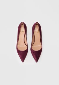 Ζευγάρι μπορντό σουέτ ψηλές στιλέτο με μπεζ εσωτερικά και χρυσά λογότυπα καρδιάς "Love Moschino" στο εσωτερικό.