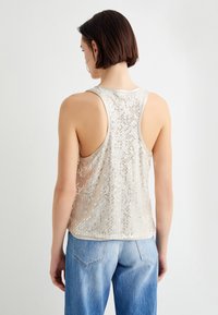 Ærmeløs beige top med et glitrende paljettmønster, letvægtigt stof, rundet kant og racerback-design, parret med denim jeans.