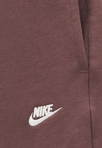 Κοντινό πλάνο καφέ υφάσματος με λευκό κεντημένο λογότυπο Nike και ορατή ραφή.