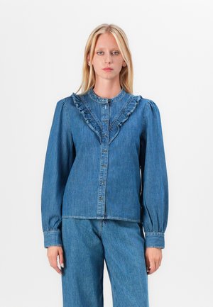 Denim topp med en volangkrage, knapplukking og lange pufferm. Stoffet er blått med en glatt tekstur.