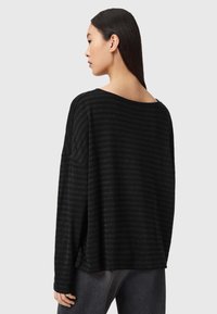 Top negru cu mânecă lungă, cu o croială lejeră, având dungi orizontale subtile, un decolteu larg și slituri laterale la tiv.