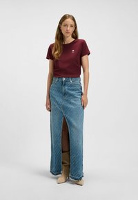 Maroon t-shirt with small heart logo, paired with a high-slit denim skirt featuring blue tones and frayed hem, worn with beige ankle boots.