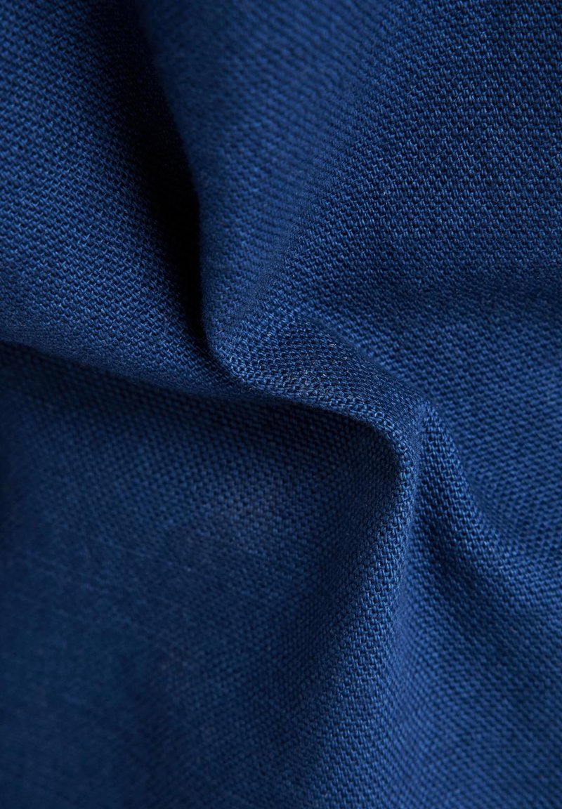 Zbliżenie na teksturowany niebieski materiał z widocznym wzorem tkania i delikatnymi fałdami tworzącymi miękkie cienie i refleksy.