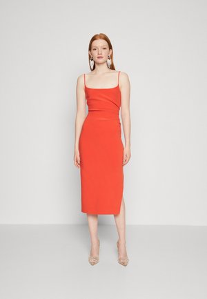 Red midi dress with thin straps, fitted silhouette, and a side slit. Worn with clear heels. Simple design, smooth texture.