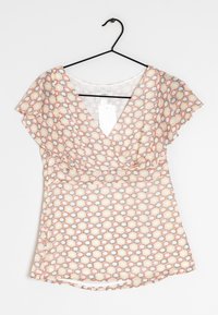 Blouse à manches courtes avec un col en V, présentant un motif géométrique en nid d'abeille dans des tons de rouge, jaune et gris sur un fond clair.