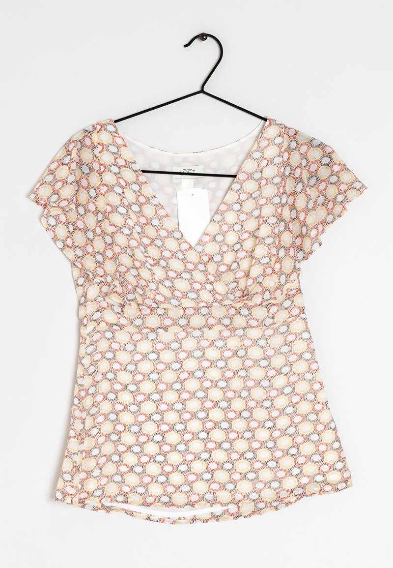 Blouse à manches courtes avec un col en V, présentant un motif géométrique en nid d'abeille dans des tons de rouge, jaune et gris sur un fond clair.