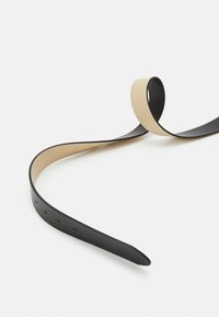 Zwarte en beige leren band, plat ontwerp, licht gebogen met gelijkmatig verdeelde gaten, gladde textuur, taps toelopend uiteinde voor het vastmaken.