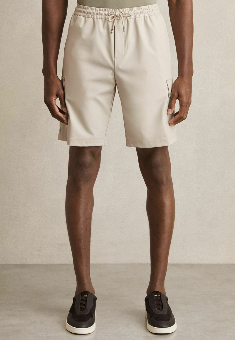 Beige Cargo-Shorts mit elastischem Bund und Kordelzug, ausgestattet mit Seitentaschen. Glattes Material mit lockerer Passform.