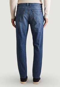 Jeans de mezclilla azul con un corte recto, que cuentan con bolsillos traseros y costuras en contraste. Llevados con zapatos negros y un suéter crema.