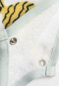 Tessuto bianco con una consistenza morbida, cinghie azzurro chiaro e bottoni metallici. Presenta un motivo giallo e verde sullo sfondo.