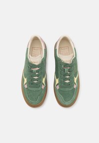 Zapatillas de ante verde con un interior crema, acentos en amarillo y rosa, punta redonda y suela de goma plana. Los cordones combinan con el material de la parte superior.