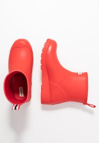 Botas de lluvia de goma rojas con una superficie texturizada, punta redondeada, talón reforzado y una tira de goma a rayas en la parte posterior.