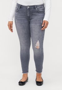 Jeans ajustados em denim cinza desbotado, com um rasgo no joelho direito, bainhas desfiadas e design de cinco bolsos. Combinados com sapatos pretos planos.
