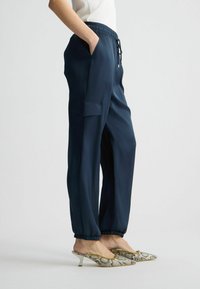 Pantalons légers bleu marine avec une taille élastique, des poches latérales et des chevilles fuselées. Portés avec des mules à bout pointu à motifs.