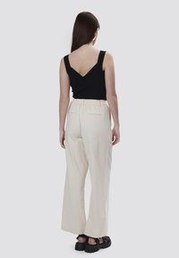 Top scollato nero a righe con schiena a V, abbinato a pantaloni larghi a vita alta color crema con tessuto testurizzato e tasche. Sandali neri.