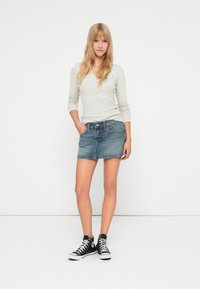 Denim mini seelikfranse äärega, kombineeritud heleda halli pikakäiselise henley särgi ja mustade kõrgete tennisetossudega. Sile tekstuur, mugav disain.
