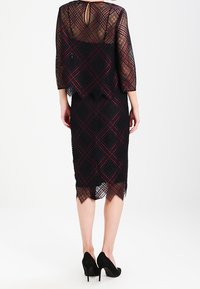 Svart spetsklänning med ett geometriskt diamantmönster, trekvartslånga ärmar och nyckelhålsrygg. Har en figursydd silhuett och scalloped nederkant.