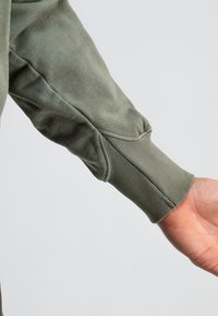 Lange mouwenshirt van olijfgroene stof, met ribgebreide manchetten en subtiele stikseldetails. Glad textuur met een ontspannen pasvorm.