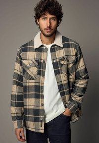 Karierte Jacke in Beige und Marineblau, aus strukturiertem Stoff. Verfügt über einen flauschigen Kragen, zwei Brusttaschen und Knopfverschlüsse.