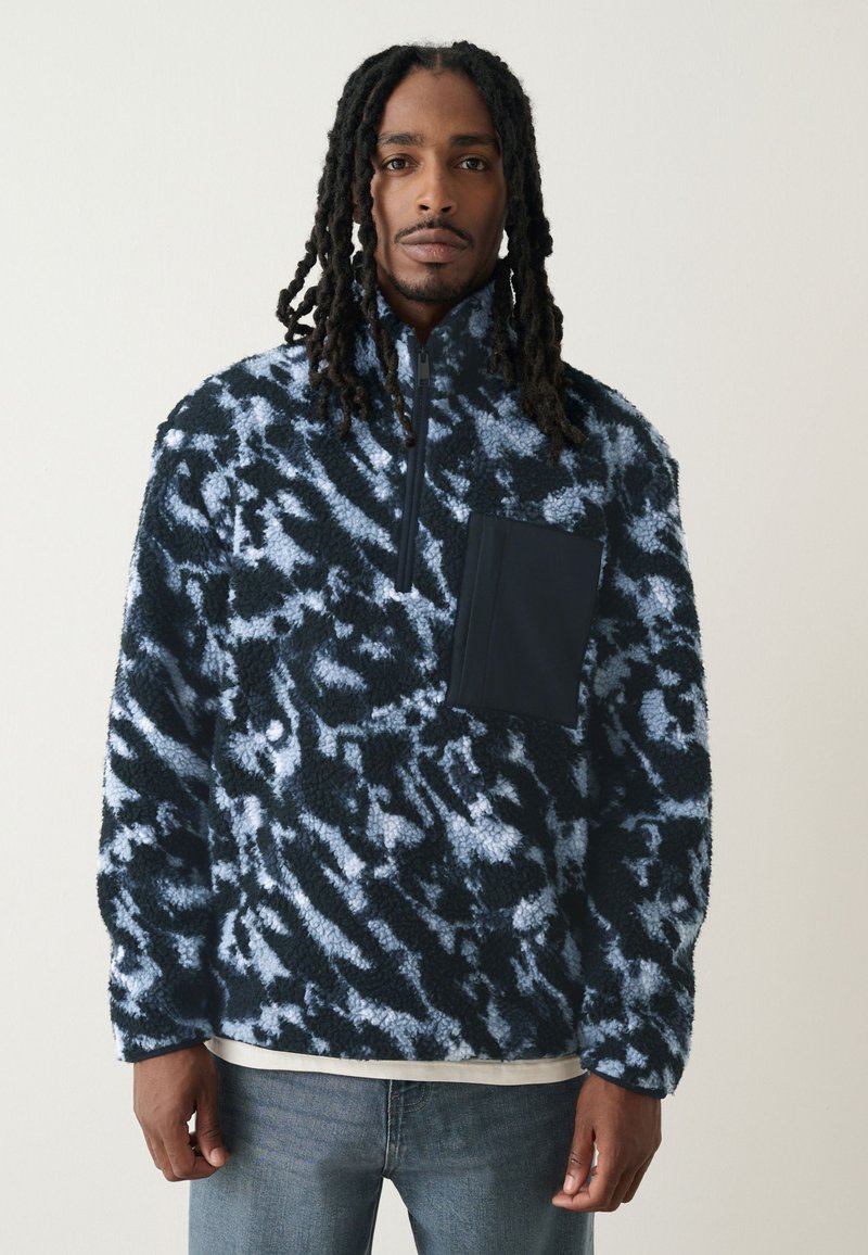 Blauwe en zwarte fleece trui met abstract patroon, hoge kraag, halve rits aan de voorkant en een borstzak in effen zwart. Gestructureerde stof.