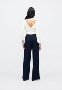 Marineblå vide bukser kombinert med en hvit langermet topp med dyp V-utringning bak og innsvingt midje, glatt stoff og knappelukking.