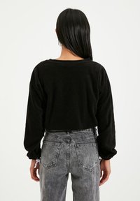 Maglione cropped nero con maniche lunghe, realizzato in tessuto morbido. Abbinato a jeans in denim grigio a vita alta con tasche posteriori e una texture sbiadita.