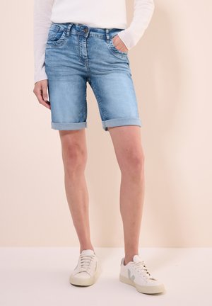 Shorts in denim azzurro con risvolti, cinque tasche e chiusura anteriore a bottone, indossati con sneakers bianche su uno sfondo neutro.
