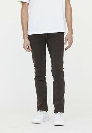 Jeans slim fit marron foncé en coton, avec un design classique à cinq poches et une texture lisse. Portés avec un t-shirt blanc ample.