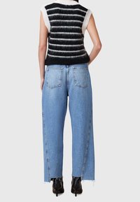 Strikket vest i sort og hvid strib, parret med lyseblå jeans med vidde, der har rå kant og baglommer, båret med sorte høje støvler.