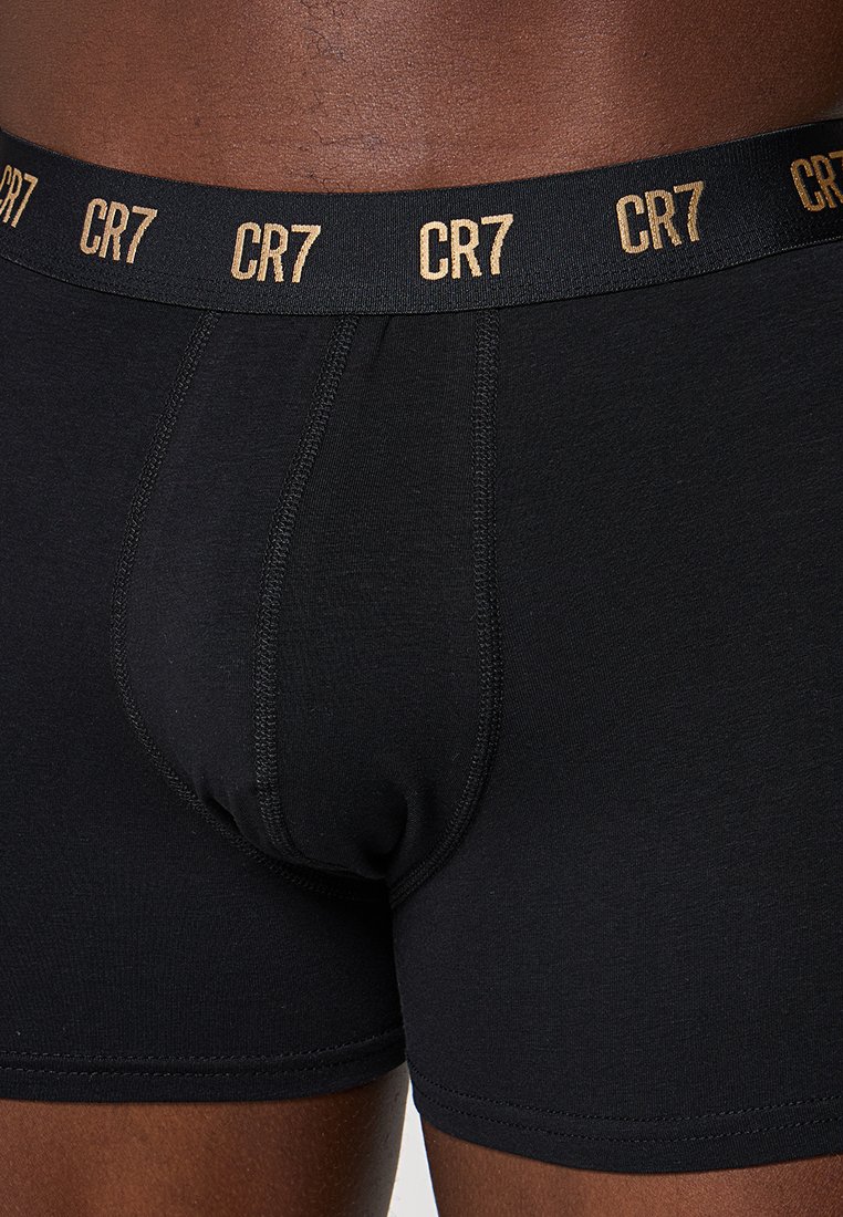 Taille und Oberschenkel, die schwarze Boxer-Shorts tragen, mit "CR7" in Gold auf dem Bund gedruckt.