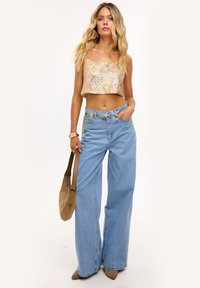 Geknipte, glanzende pailletten top in pastelkleuren; wijde lichtblauwe jeans; beige tas; spitse beige hakken; opvallende hardware accenten.