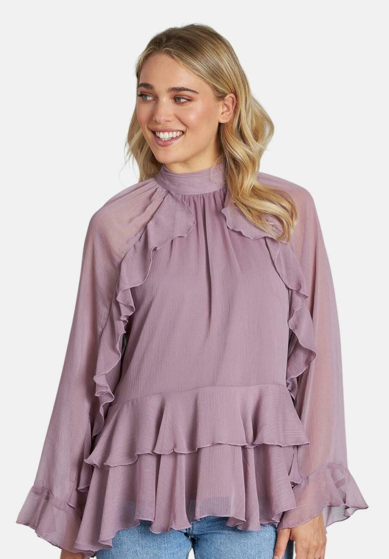 Blusa lavanda con dettagli arricciati, colletto alto e maniche lunghe, caratterizzata da un orlo a strati. Realizzata in tessuto leggero e testurizzato.
