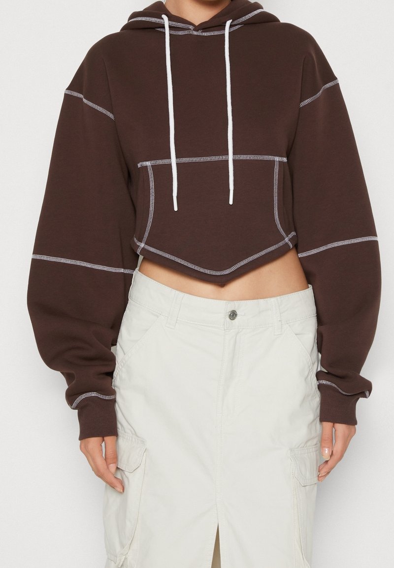 Brown cropped hoodie with white drawstrings, contrast stitching, and a front pocket, paired with a white cargo skirt.