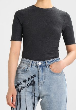 Osoba ubrana w dopasowany, ciemnoszary krótki rękaw i jasnoniebieskie dżinsy z wyhaftowanym na udzie napisem "Nie ma miejsca jak Ziemia" czarną nicią.