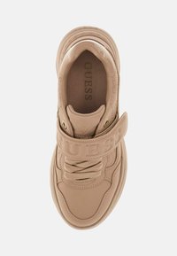 Beżowe sneakersy Guess z grubą podeszwą, sznurowaniem z przodu i szerokim paskiem na górze z wytłoczonym logo "GUESS", widok z góry.