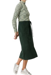 Vihreä samettinen midihame, jossa on vyötäröllä nauha, yhdistettynä kuviolliseen pitkähihalaiseen puseroon ja hopeisiin tennareihin. Sileä pinta, yksinkertainen muotoilu.