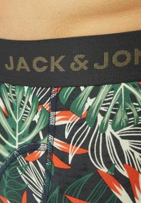 Boxershorts met een zwarte tailleband met de tekst "JACK & JONES". De stof toont een levendig tropisch bladpatroon in groen en rood.
