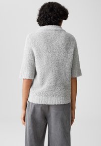 Maglione corto a maniche corte grigio e peloso con scollatura rotonda e tessuto testurizzato, abbinato a pantaloni di velluto a coste grigi chiari.