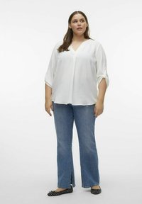 Vit, lätt blus med V-ringning och uppvikta trekvartsärmar, i kombination med ljusblå utsvängda jeans och svarta mönstrade ballerinas.