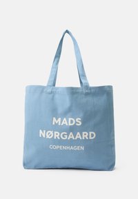 Jasnoniebieska torba na ramię z płótna z białym napisem "MADS N�ØRGAARD COPENHAGEN" i dwoma solidnymi ramiączkami na ramię.