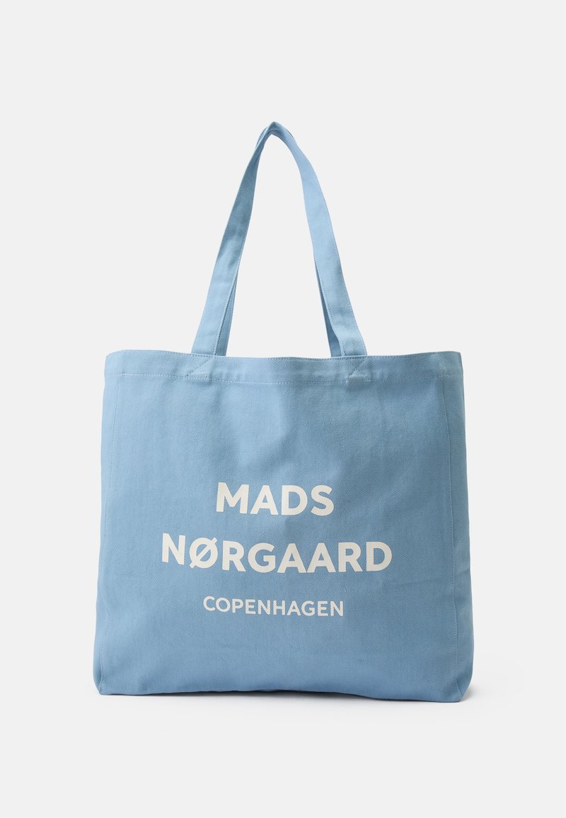 Jasnoniebieska torba na ramię z płótna z białym napisem "MADS NØRGAARD COPENHAGEN" i dwoma solidnymi ramiączkami na ramię.
