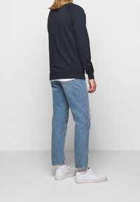 Marinblå sweatshirt med ribbade muddar, kombinerad med ljusblå raka jeans och vita sneakers. Enkel och avslappnad design.