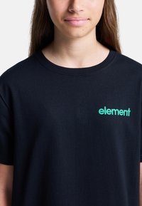 Czarna bawełniana koszulka z okrągłym dekoltem, z zielonym logiem "element" na lewej piersi. Krótkie rękawy, gładka tekstura.