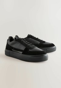 Schwarze Sneakers aus Leder und Wildleder mit einem Low-Top-Design, flachen Schnürsenkeln und einer strukturierten Gummisohle mit glatt verarbeitetem Finish.