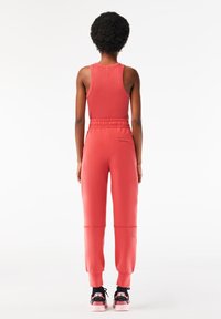 Korallfärgad sportoutfit med en ärmlös topp och tapered joggers med elastisk midja. Texturerad tyg och kontrasterande skor.